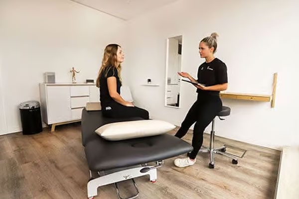 Therapeutin im Gespräch mit einer Patientin auf einer Liege bei myPhysio Deutschland.